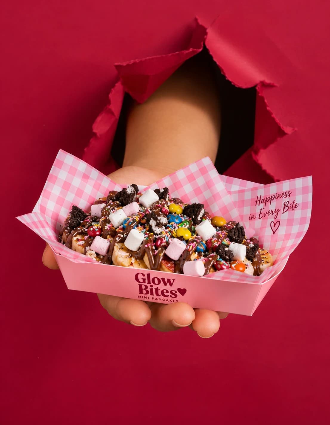 A Glow Bites box of mini pancakes with marshmallows, chocolate and candy, held out through torn red paper